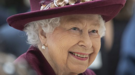 The Queen wears a burgundy-coloured hat and smiles