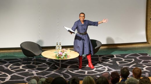 Adjoa Andoh stands with her arms apart as she delivers a lecture in front of an audience.