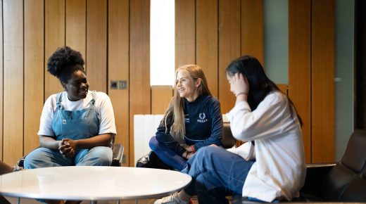 Three students sit around a table and talk.